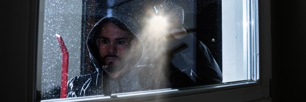 man peering into window with flashlight at night