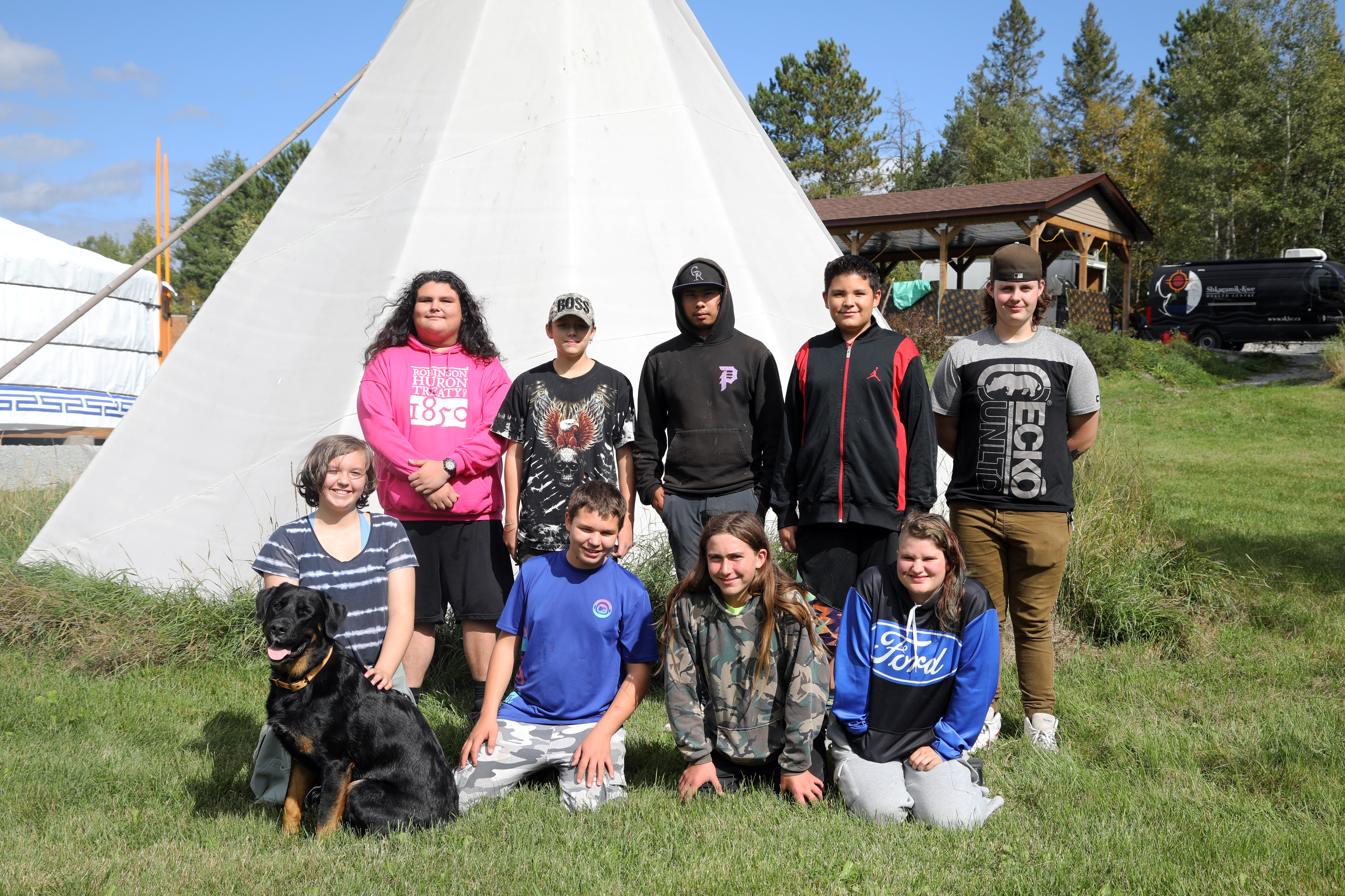 youth smiling outside with dog in front of tipi