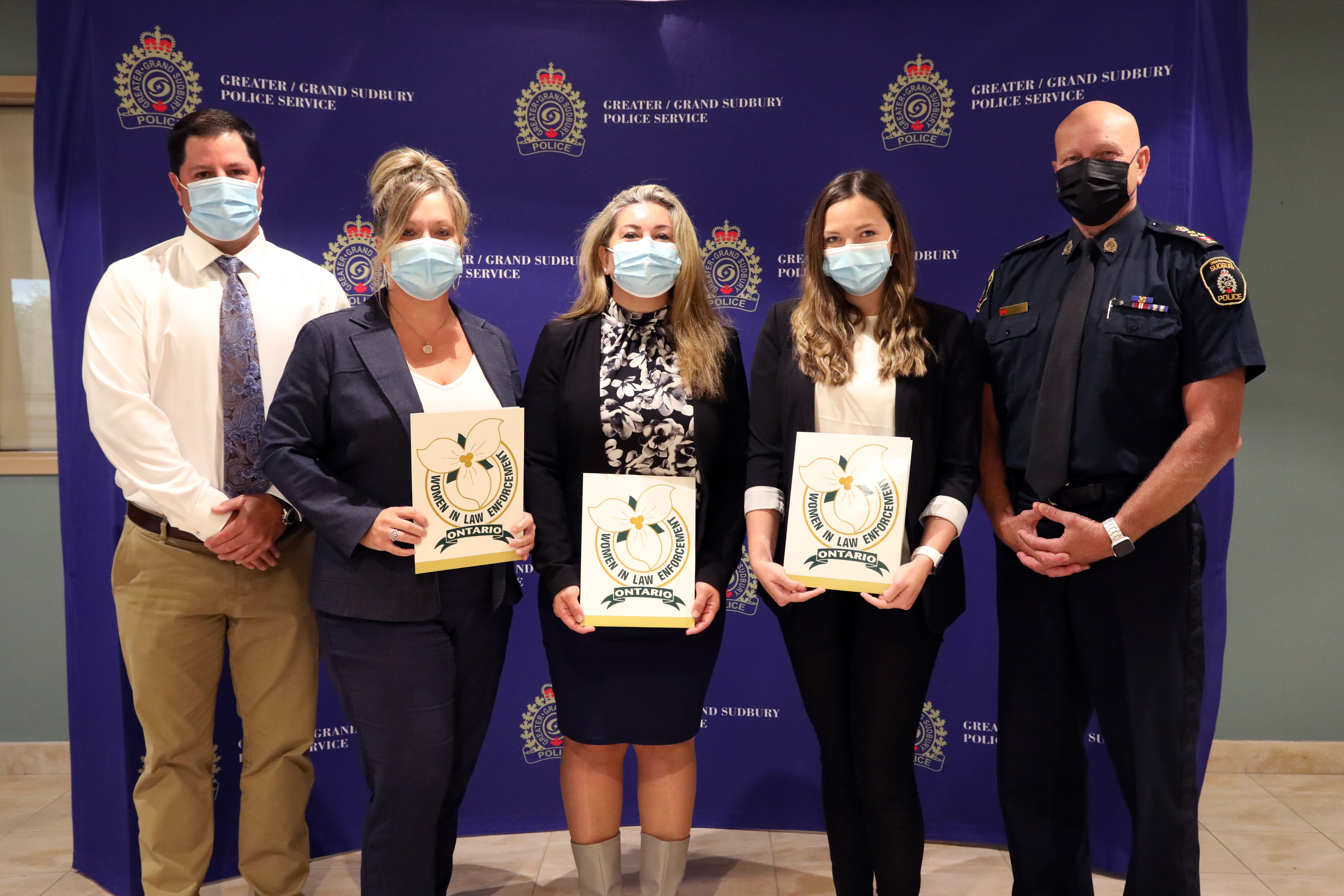 five people wearing masks standing and holding certificates