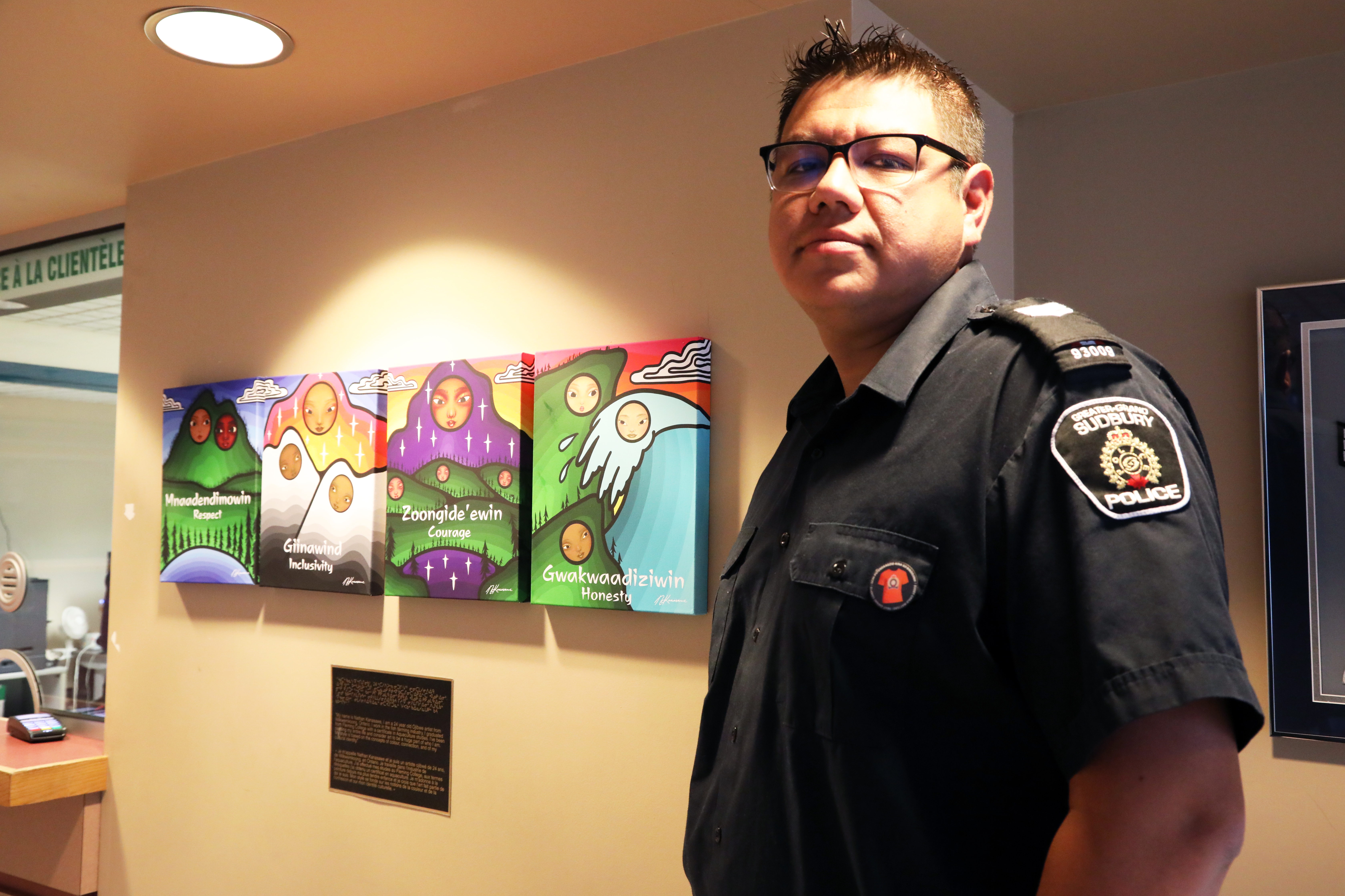 Officer wearing orange pin standing in front of Indigenous art work