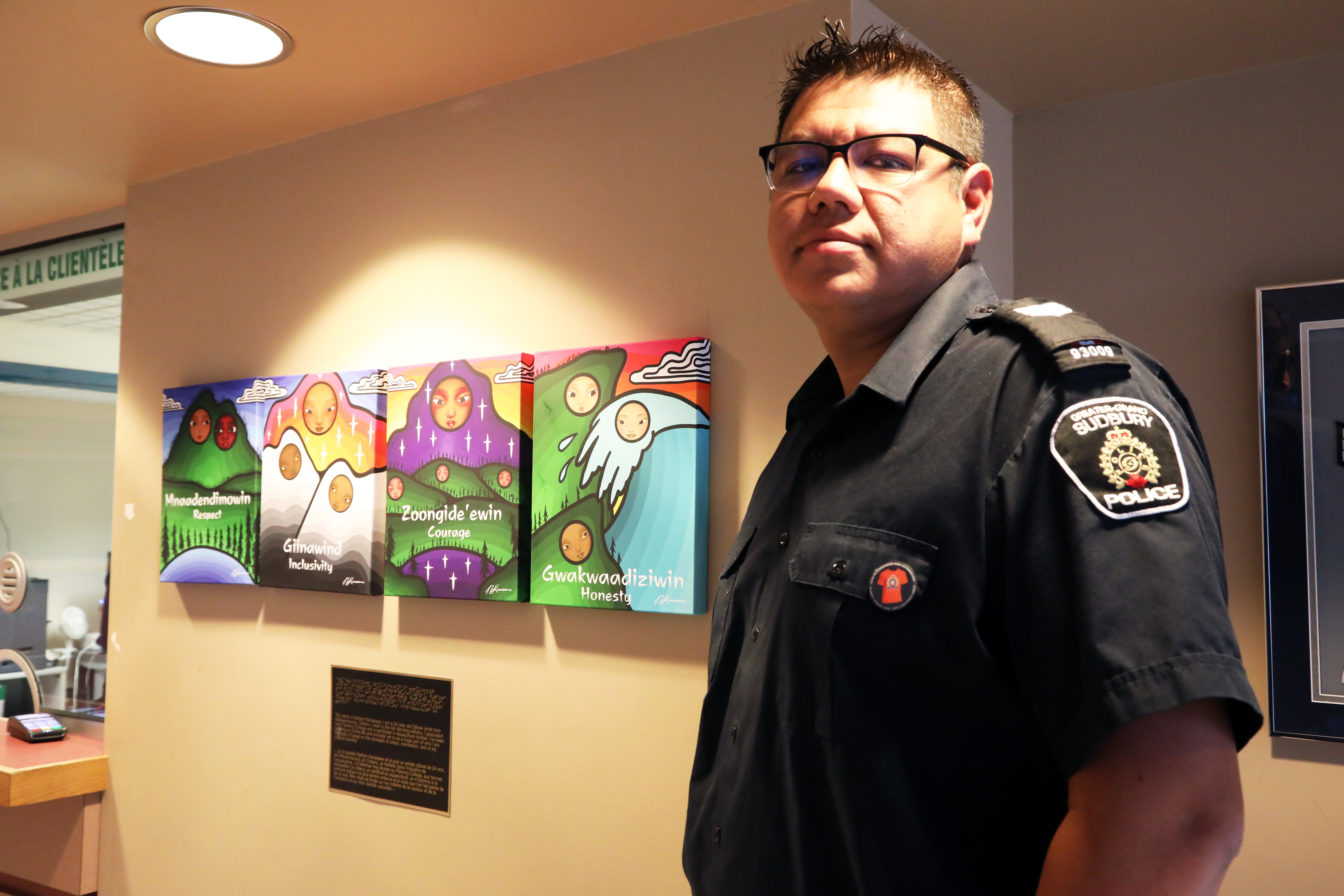 Officer wearing orange pin standing in front of Indigenous art work