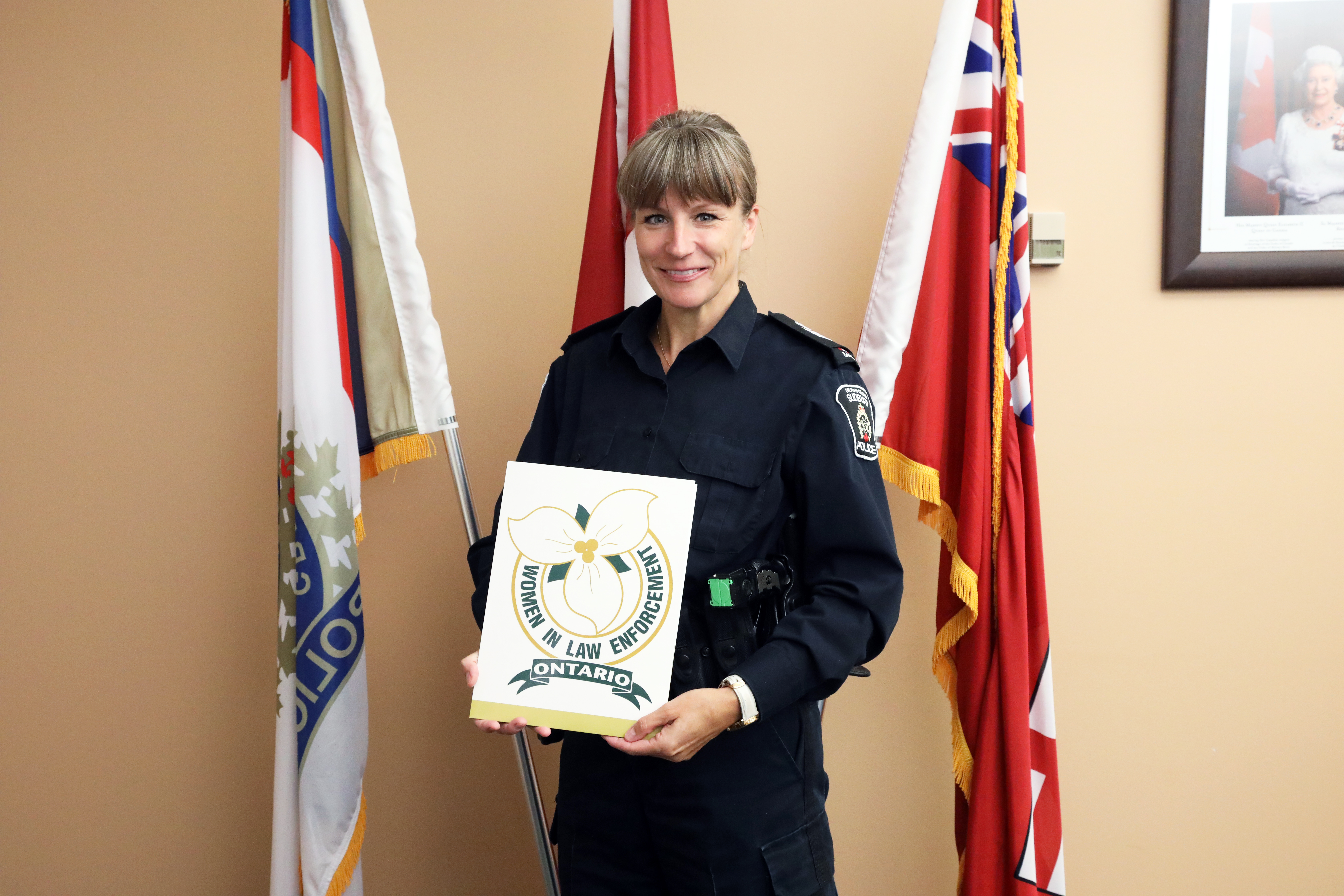 police officer standing in front of flags holding nomination certificate