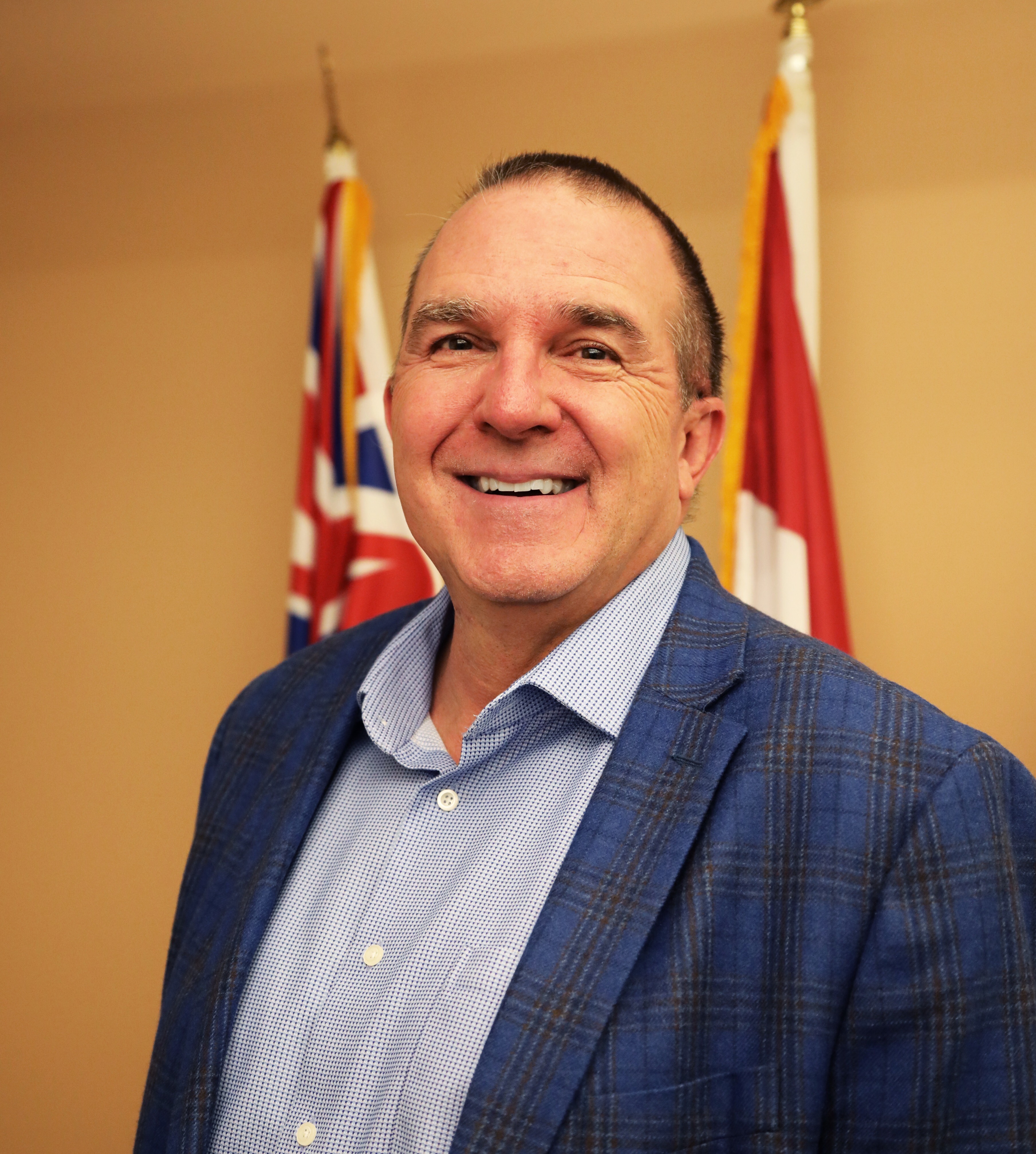 man in suit standing in front of flags and smiling