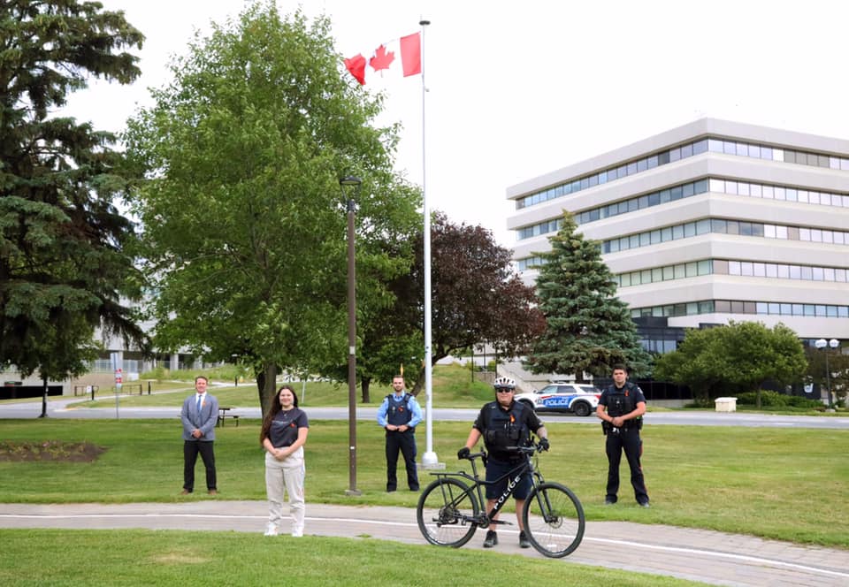 people wearing orange ribbons standing in front of Canadian flag