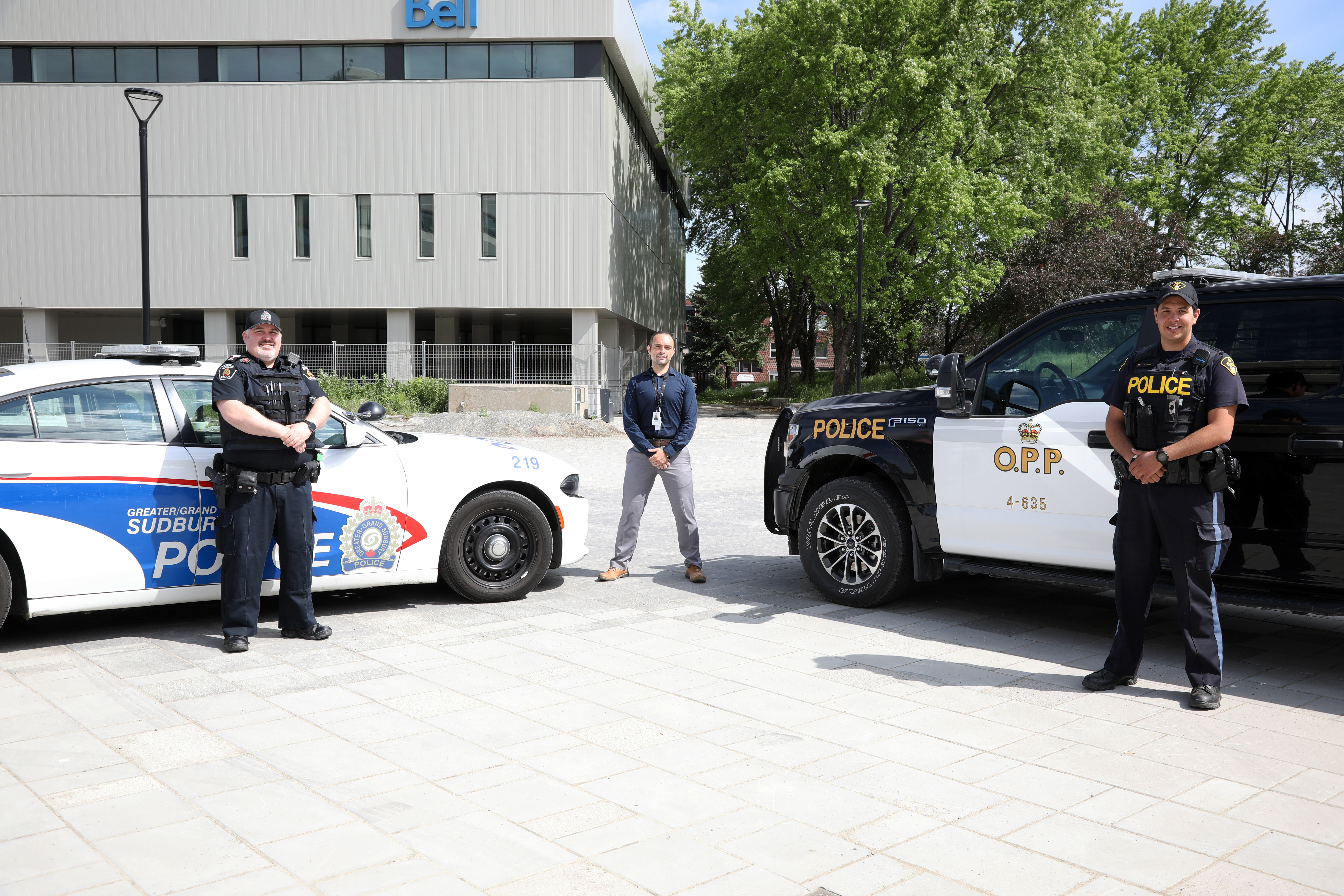 Two police officers and health representative standing between police cruisers