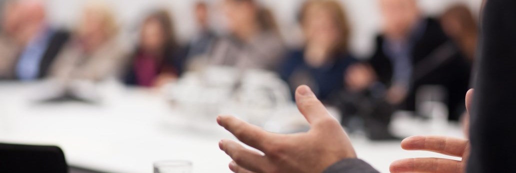 person talking with their hands to a group of blurred people